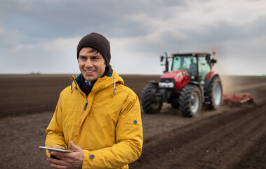 Farmer with tablet in front of tractor in field
