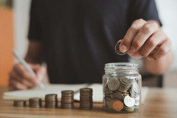 Businessman in a black shirt sat writing financial notes, accounts with stack coins on their desks at office. Save money for future investments, financial growth concept
