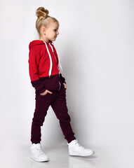 Kid in red warm overalls, white sneakers walking along the studio wall. Full-length portrait. Children's fashion, casual wear, comfortable children clothing for winter and autumn