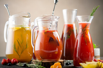 A set of various jugs with lemonades and natural juice of fruits and berries. Colorful cocktails, with fresh fruit, on a black stone background.