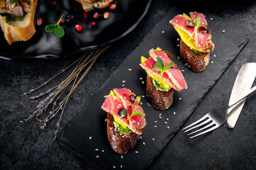 Bruschetta with tuna, avocado and sesame seeds on black stone. Italian Antipasti and snacks