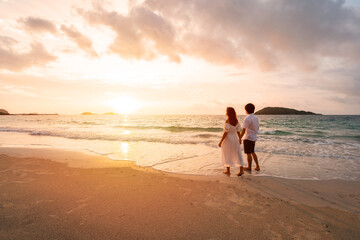 Young woman traveler holding man's hand and looking beautiful sunset on the beach, Couple on vacation in summer concept