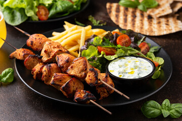 Chicken fillet souvlaki, kebabs on skewers with potato chips, salad and fresh home made tzatziki