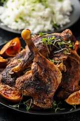 Slow cooked aromatic duck legs with basmati rice and orange wedges on black plate