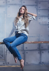 Fototapeta na wymiar Portrait of young beautiful blonde woman is sitting on a board on smoke and metal wall background.