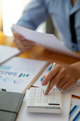 Close up of Business using calculator and laptop for doing math finance report on wooden desk, tax, accounting, statistics and analytical research concept