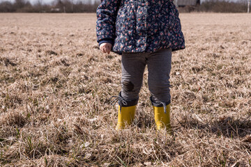 a little girl runs and plays in the field in the spring. a child in rubber boots plays with a stick