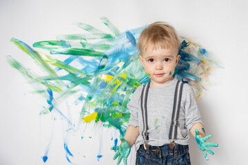 Little child got his hands dirty with paints and painted on a white wall. Happy childhood