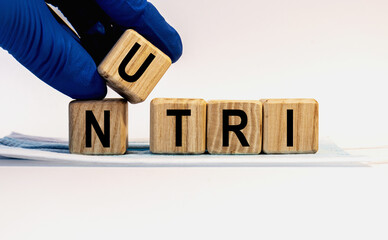 Text NUTRI made from wooden cubes. Hands in a blue glove.