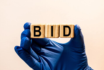 The word BID which is made from wooden cubes. Hands in a blue glove. Isolated on WHITE background