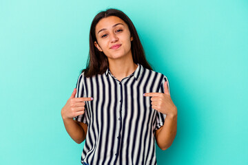 Young Indian woman isolated on blue background person pointing by hand to a shirt copy space, proud and confident