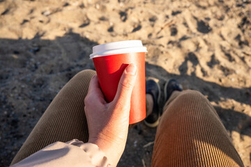 Coffee in a disposable red cup in the hands of the girl.