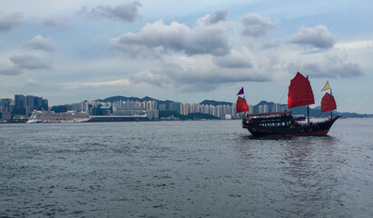 Traditional Chinese junk with red sails in Victoria Harbor, Hong Kong in China with panoramic city...