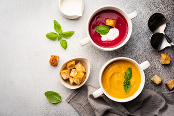 Vegetarian beetroot and pumpkin cream soups in a bowls with croutons on a gray background, top view