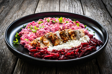 Marinated herring fillets in cream with roast beetroots, pickled cucumber, boiled potatoes, parsley, onion and apple on wooden table
