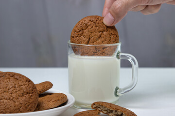 Oatmeal cookies dipped in a glass of milk on a white background. Diet food. Light breakfast