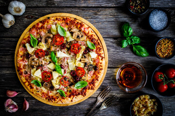 Pizza capricciosa with white mushrooms, ham, artichoke, tomatoes, olives, parmesan and mozzarella on wooden background
