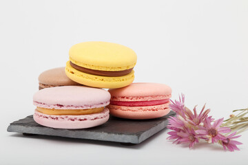 Colorful macaroons on grey mat on white background. Sweet bakery with dry immortelle flowers, copy space.