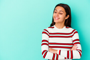 Young Indian woman isolated on blue background smiling confident with crossed arms.