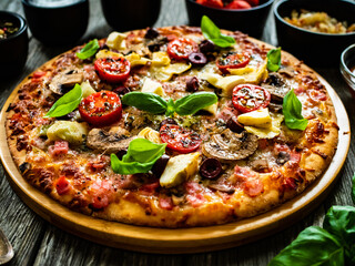 Pizza capricciosa with white mushrooms, ham, artichoke, tomatoes, olives, parmesan and mozzarella on wooden background
