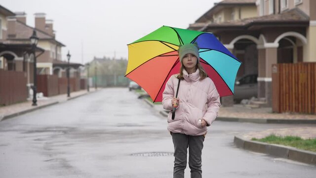 Portrait of a girl with an umbrella in the cityscape7 A child in a hat jacket jeans and sneakers stands on the street in a new neighborhood with beautiful architecture.
