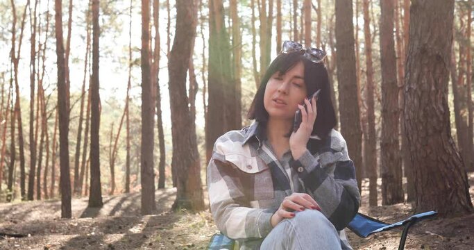 Bussiness woman having phone call, speking, sitting in chair in pine forest in sun shine spring day, relaxation and healthy lifestyle concept, get outside.