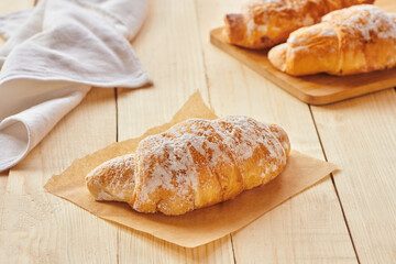 Tasty croissants with powdered sugar on wooden board. Traditional french pastry on the breakfast. Close up view
