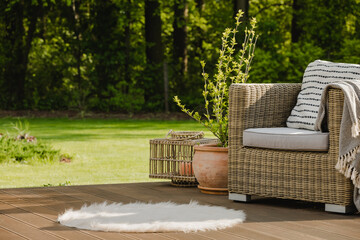 Wicker armchair with pillow on green terrace in beautiful garden - obrazy, fototapety, plakaty