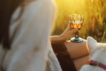 Wine glass in woman hand close up on background of summer meadow grass in warm sunset light. Picnic