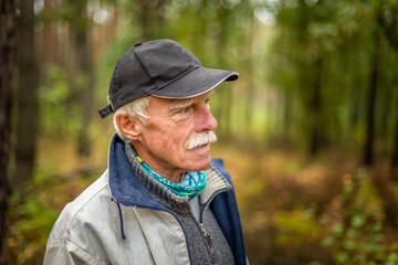 Naklejka na ściany i meble A mature man wearing a cap walking in the woods during the day.