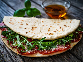 Italian piada wraps - piadina stuffed with fresh vegetable leaves and salami sausage on wooden table
