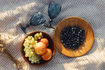 Summer picnic. Fresh  fruits in wooden plates and wineglasses on  blanket in sunny light in meadow