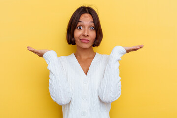 Young mixed race woman isolated on yellow background doubting and shrugging shoulders in...