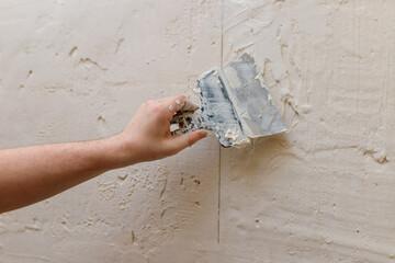 Male hands with spatula using putty for wall, builder making overhaul.