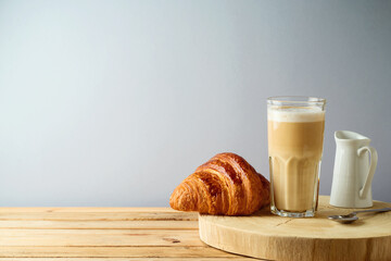 Coffee cup and croissant on wooden table over gray background