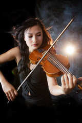 Fototapeta premium An Asian young woman is playing violin. Violinist is performing on the stage. Her hair flying in contour light. Emotional. Musical Instrument 