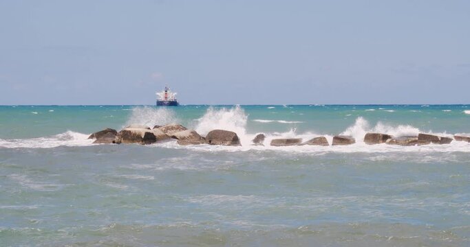 View of a container ship from the Bari seafront with the rough sea breaking the waves on the rocks