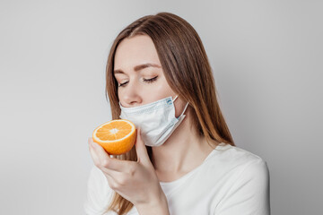 Loss of smell concept. Caucasian young woman in a medical mask sniffing an orange on a white background in the studio