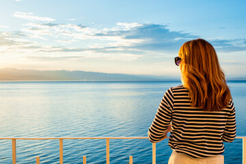 Fototapeta premium Rear view of woman standing on the balcony and enjoying the sea view