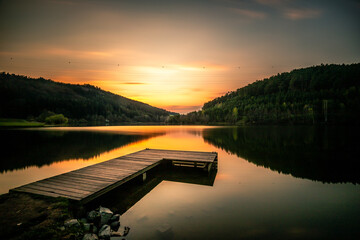 View of a lake in the sunset. A great wooden jetty on a natural lake in the forest. swim and fish - obrazy, fototapety, plakaty