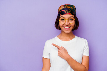 Young mixed race woman wearing a bandana isolated on purple background smiling and pointing aside, showing something at blank space.