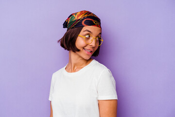 Young mixed race woman wearing a bandana isolated on purple background looks aside smiling, cheerful and pleasant.