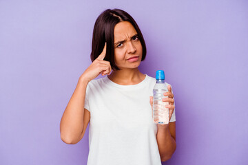 Young mixed race holding a water bottle isolated on purple background pointing temple with finger, thinking, focused on a task.