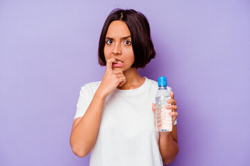 Young mixed race holding a water bottle isolated on purple background biting fingernails, nervous and very anxious.