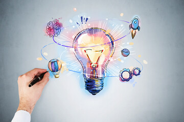 Businessman hand drawing colorful light bulb as a concept of new idea for start up. Concept of creativity and brainstorming. Light blue wall on background © ImageFlow