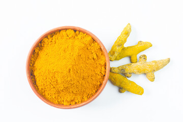 Dry turmeric or haldi powder in a earthen bowl with turmeric roots on white isolated background.
