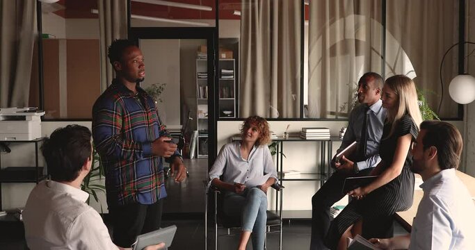 Happy young skilled african ethnicity manager speaking talking presenting business project idea to interested multiracial diverse colleagues during informal communication in modern office workplace.