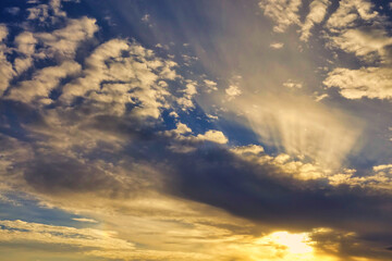 Fototapeta premium Blue sky with clouds and sunbeams at sunset