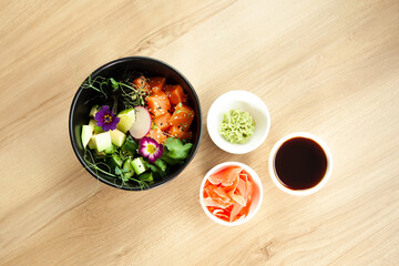 Poke salad with salmon in a bowl next to wasabi and ginger. Ingredients fresh salmon, avocado, cucumber, rice, Tamarind sauce, mango sauce, nori lime sesame seeds cilantro. Asian seafood salad concept