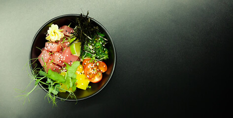 Poke salad with tuna in a bowl. Ingredients fresh tuna, cherry tomatoes, marinated seaweed, rice,...